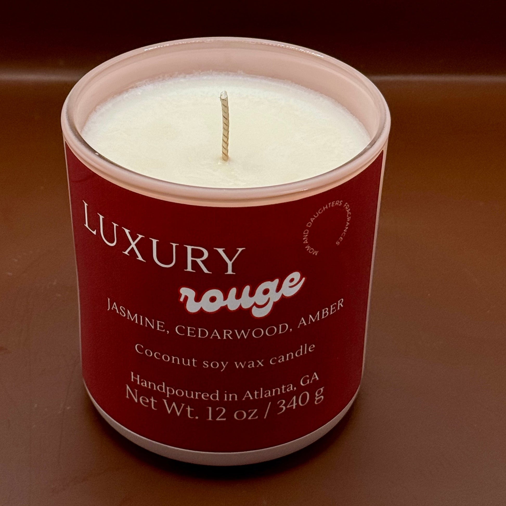 A textural image of a luxury rouge candle with a glowing flame, surrounded by a warm, inviting ambiance. Text overlay reads: "Introducing our new luxury rouge candle - the ultimate indulgence for candle lovers. Slow-burning formula fills your home with opulent fragrance. Perfect for unwinding or creating romantic ambiance. Order yours today!