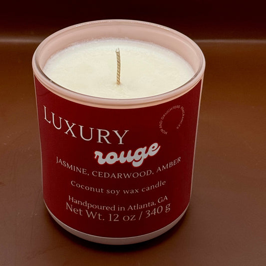 A textural image of a luxury rouge candle with a glowing flame, surrounded by a warm, inviting ambiance. Text overlay reads: "Introducing our new luxury rouge candle - the ultimate indulgence for candle lovers. Slow-burning formula fills your home with opulent fragrance. Perfect for unwinding or creating romantic ambiance. Order yours today!